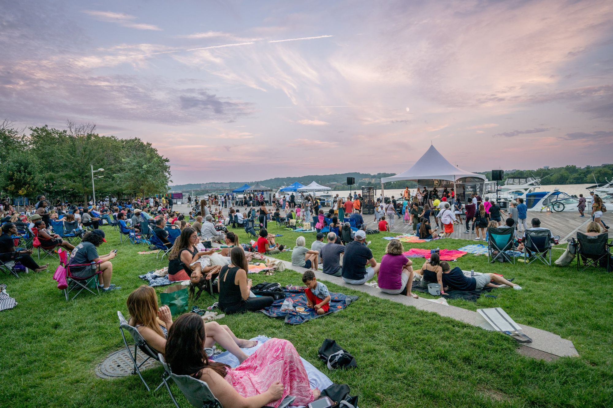 Crowds on picnic blankets and lawn chairs at an evening concert on the Georgetown waterfront