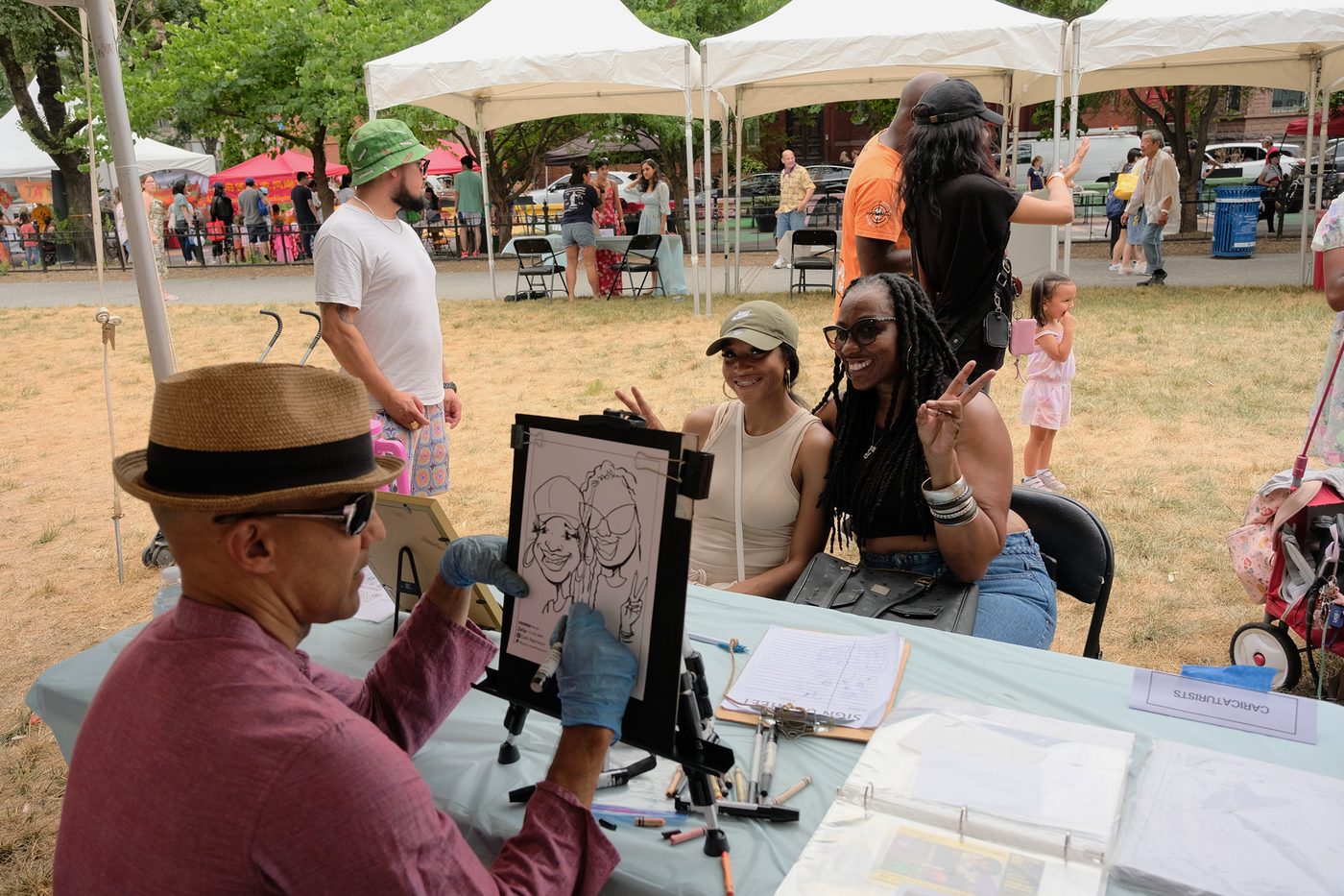 A caricature artist sketching two smiling women at the Chinatown Park Festival